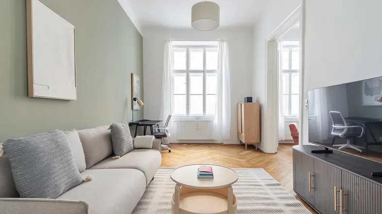 Helles Wohnzimmer mit bequemem Sofa, Schreibtischbereich und Fischgrätparkettboden.