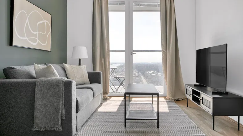 Helles Wohnzimmer mit modernem Sofa, Teppich und Zugang zum Balkon mit Stadtblick.