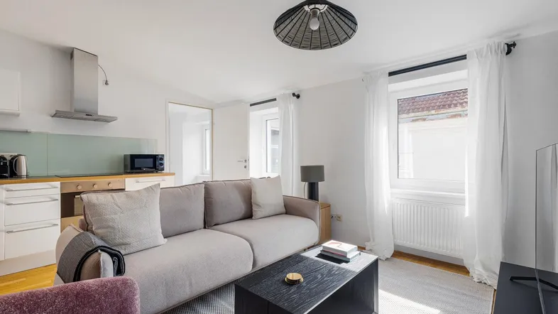 Heller offener Wohnbereich mit integrierter Küchenzeile, modernem Sofa und Blick nach draußen.