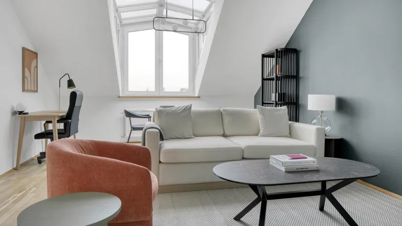 Helles Wohnzimmer im Dachgeschoss mit Schreibtischbereich, Sofa und modernem Couchtisch.