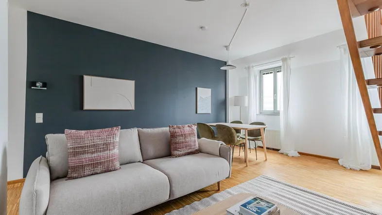 Modernes Wohn-Esszimmer mit dunkelblauer Akzentwand, Parkettboden und Holztreppe.