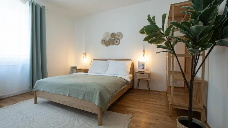 Helles Schlafzimmer mit Holzbett, Parkettboden und dekorativer Pflanze in modernem Stil.