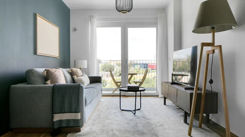 Helles Wohnzimmer mit modernem Sofa, Teppich und Zugang zu einem kleinen Balkon.