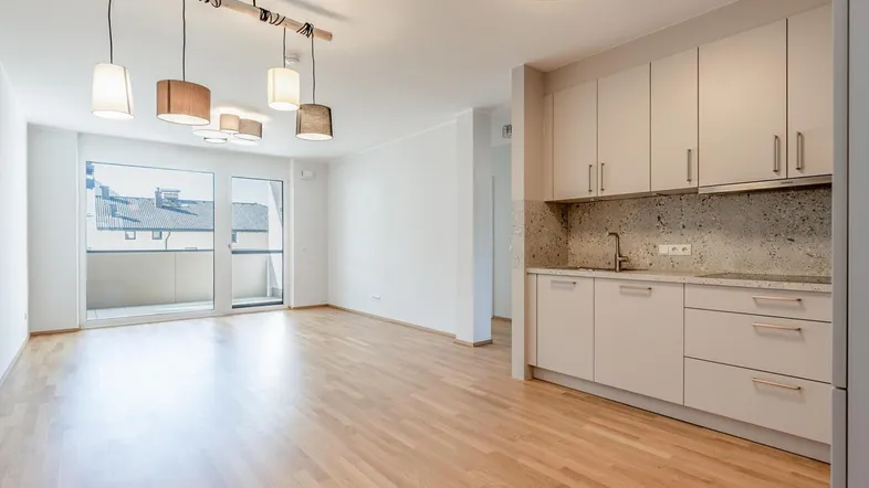Helles, offenes Wohnzimmer mit integrierter Küchenzeile und Zugang zum Balkon.