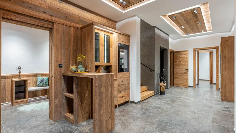 Geräumiger Eingangsbereich mit Holzelementen, Fliesenboden und indirekter Deckenbeleuchtung in modernem Chalet-Stil.