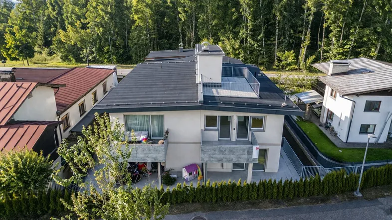 Luftaufnahme eines modernen Mehrfamilienhauses mit Balkonen, Dachterrasse und umgebender grüner Landschaft.