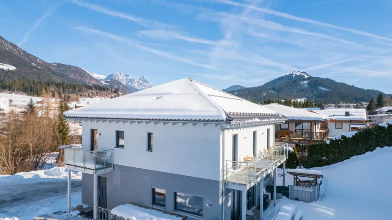 Modernes Wohnhaus in verschneiter Berglandschaft mit Balkonen und großen Fenstern.