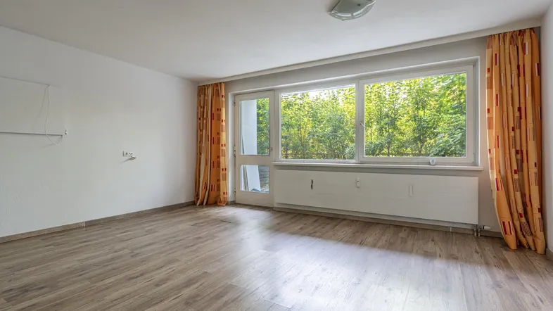 Helles Wohnzimmer mit Laminatboden und großen Fenstern mit Blick ins Grüne.