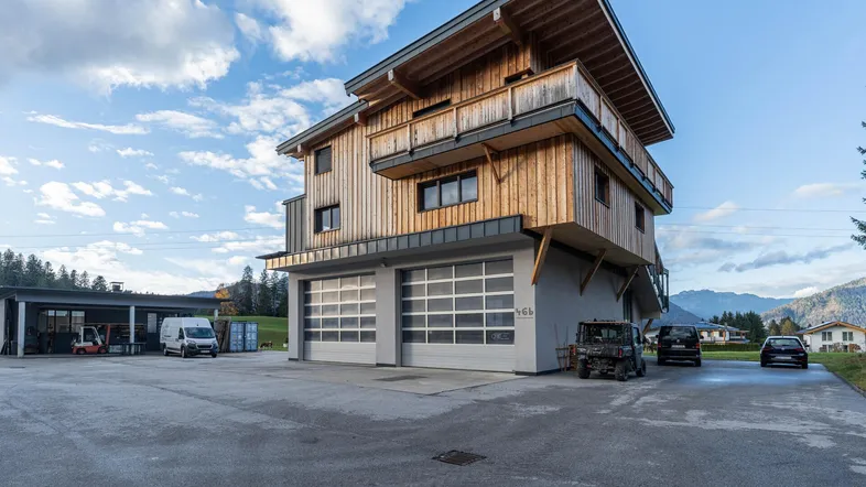 Modernes Gebäude mit Holzfassade, großen Garagentoren und umliegendem Gelände unter bewölktem Himmel.