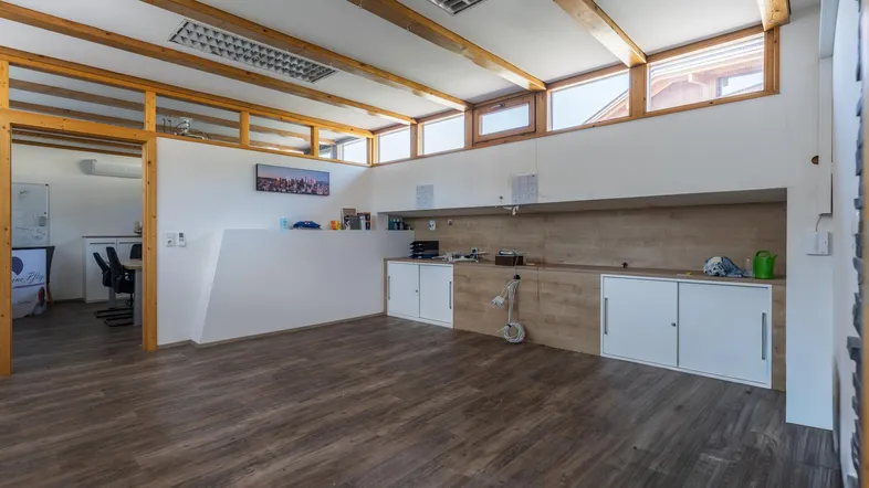 Großzügiger Büroraum mit Holzbalken, großen Fenstern und integrierten Schränken, ideal für kreatives Arbeiten.