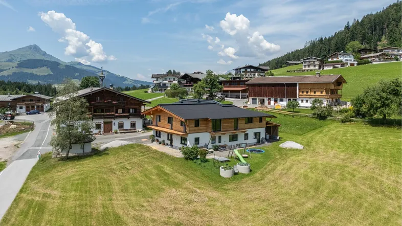 Luftaufnahme eines modernen Hauses in alpiner Umgebung mit grünen Wiesen und Bergblick.