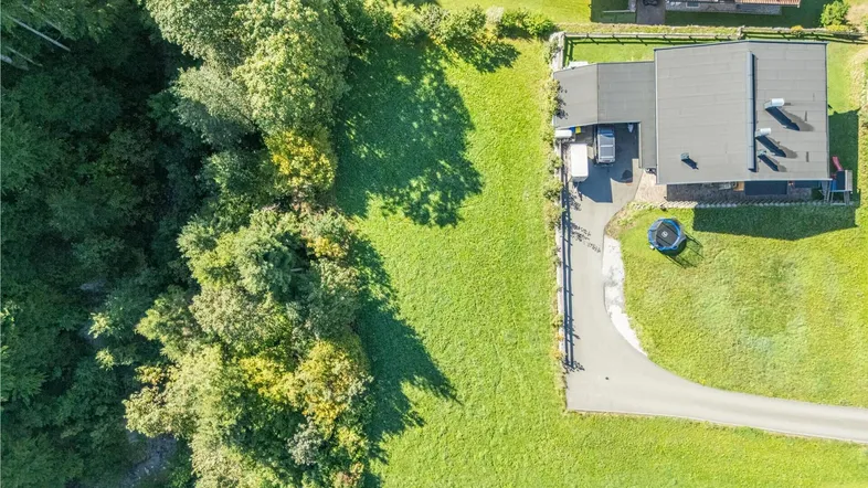 Luftaufnahme eines Anwesens mit Wohnhaus, großem Garten, Zufahrt und umgebenden Bäumen.