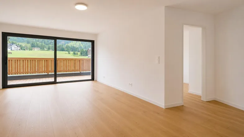 Helles Wohnzimmer mit Holzboden, großen Schiebetüren und Bergblick auf grüne Hügel.