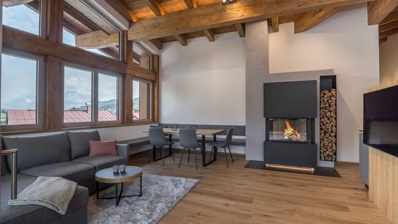 Geräumiger Wohn- und Essbereich mit modernem Kamin, Holzbalken und weitem Bergblick.