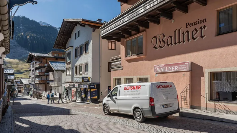 Blick auf eine belebte Straße in einem Bergdorf mit traditionellen Gebäuden und einem Lieferwagen.