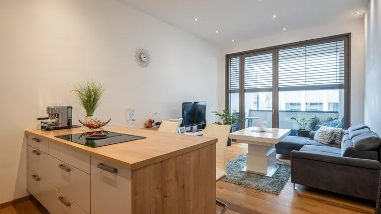 Heller offener Wohn- und Essbereich mit moderner Küche, Holzboden und Zugang zum Balkon.