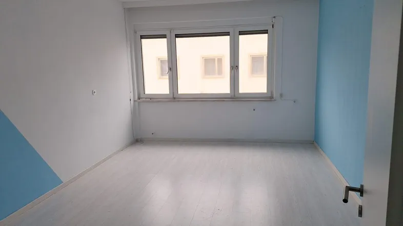 Leeres Zimmer mit hellblau gestrichenen Wänden und hellem Laminatboden, bereit zur individuellen Gestaltung.