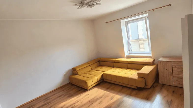 Helles Wohnzimmer mit modernem Ecksofa, Laminatboden und einem Fenster mit Tageslicht.