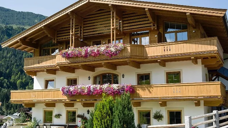 Traditionelles Chalet mit Holzbalkonen, Blumenkästen und Bergblick unter blauem Himmel.