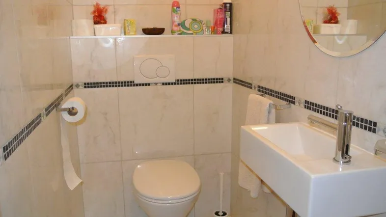 Kleines, hell gefliestes Gäste-WC mit wandhängender Toilette und modernem Waschbecken.