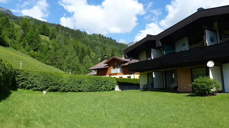Großer grüner Gartenbereich mit gepflegter Hecke und Blick auf die bewaldeten Berge unter blauem Himmel.