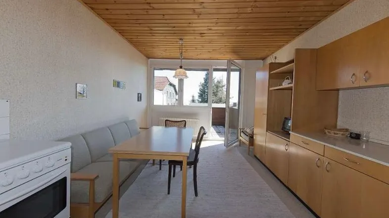 Gemütlicher Wohn-Essbereich mit integrierter Küchenzeile, Holzbalkendecke und Zugang zum Balkon.