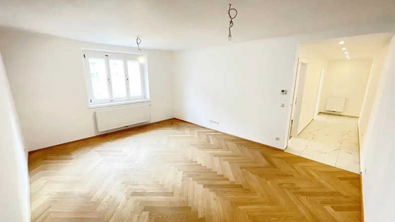 Helles, frisch renoviertes Zimmer mit Fischgrätparkettboden und weiß gestrichenen Wänden.