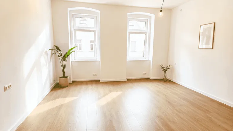Heller, leerer Raum mit Laminatboden und zwei Fenstern, ideal als Wohnzimmer.
