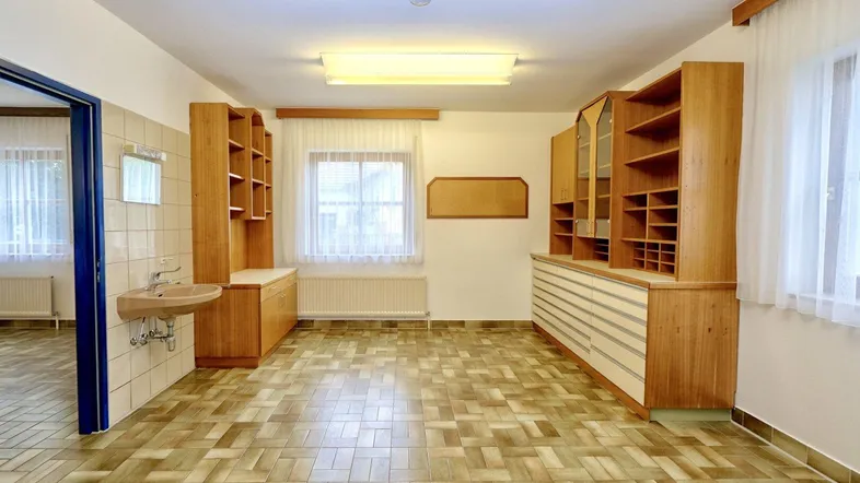 Geräumiger Büroraum mit Holzregalen, einem Waschbecken und Fliesenboden, ideal für gewerbliche Nutzung.