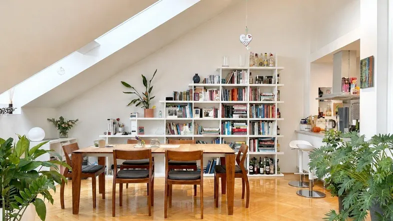 Heller Wohn- und Essbereich mit Dachschrägen, Parkettboden und integriertem Bücherregal, offen zur Küche.