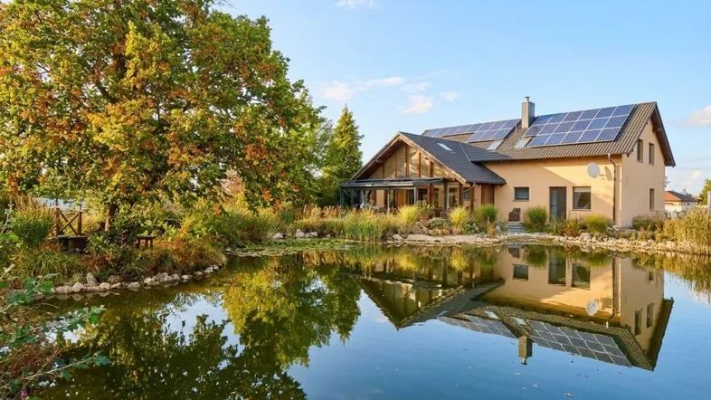 Großzügiges Einfamilienhaus mit Teich, umgeben von üppiger Natur und mit Solaranlage auf dem Dach.