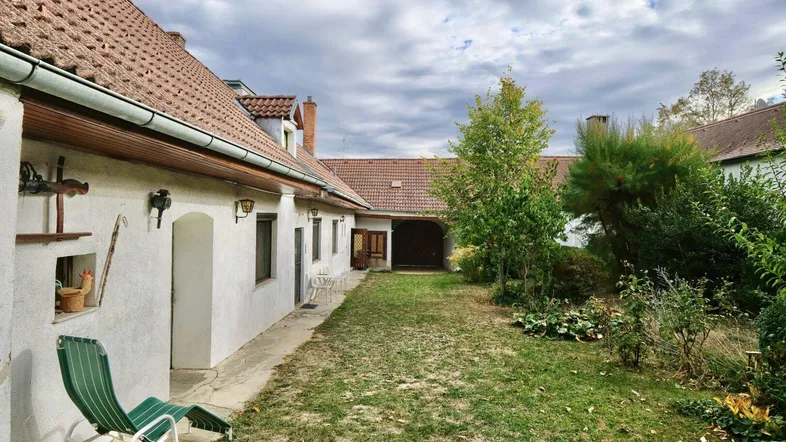 Blick auf die Gebäudefassade mit einem kleinen Gartenbereich und einer Liege im Freien.