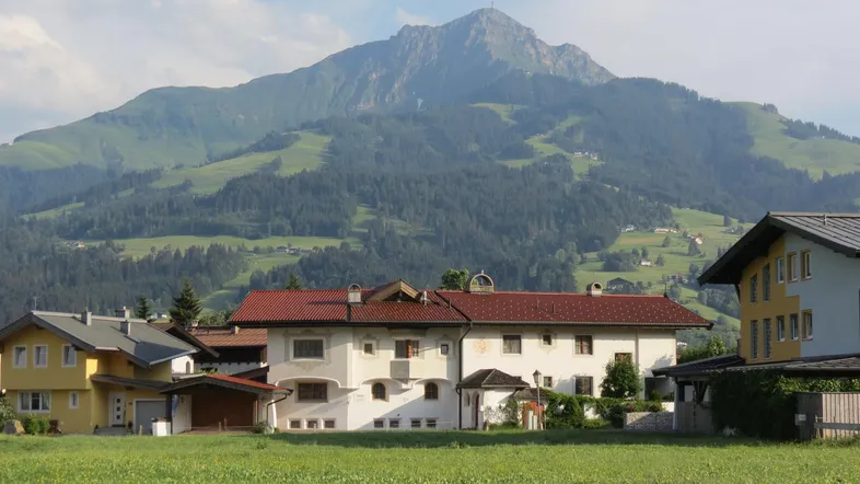 Häuser in einer ländlichen Umgebung mit einem majestätischen Berg im Hintergrund unter blauem Himmel.