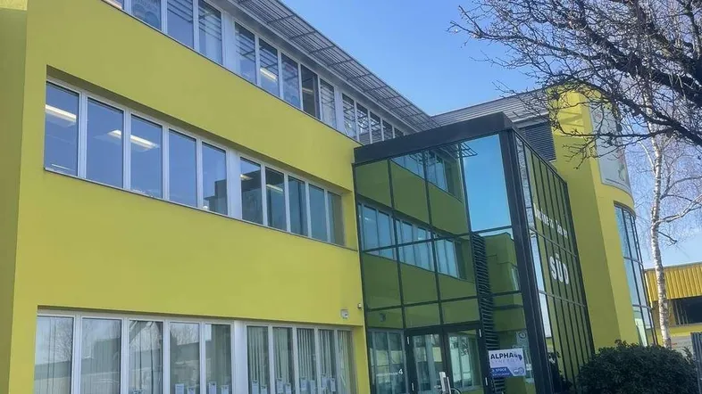 Modernes Bürogebäude mit leuchtend gelber Fassade und Glas-Eingangsbereich unter blauem Himmel.
