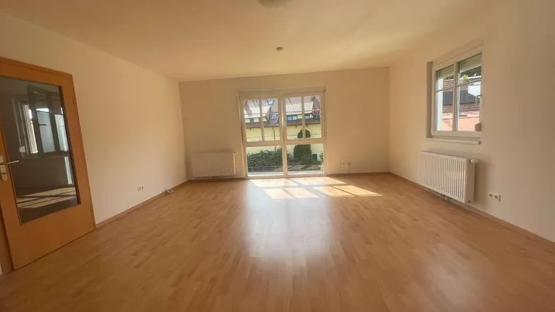 Helles Zimmer mit Parkettboden und Zugang zu einem Balkon oder einer Terrasse.