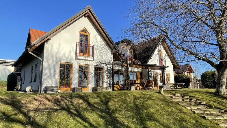 Charmantes Landhaus mit Giebeldach, großen Fenstern und einer sonnigen Terrasse mit Sitzgelegenheiten.