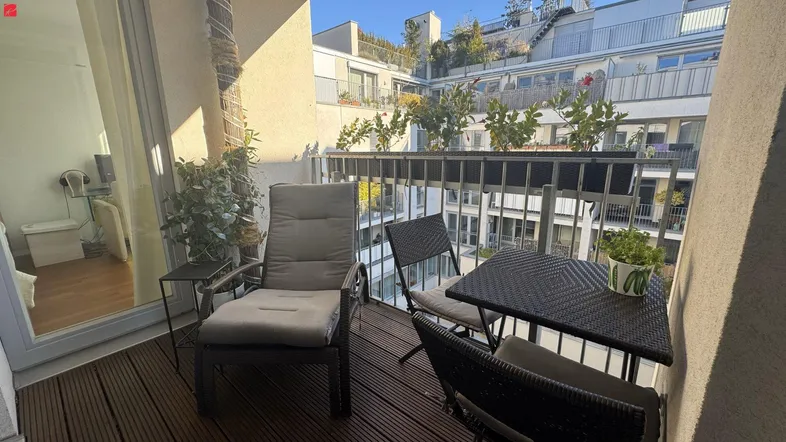 Sonniger Balkon mit Holzboden und Sitzgelegenheiten, umgeben von modernen Gebäuden.