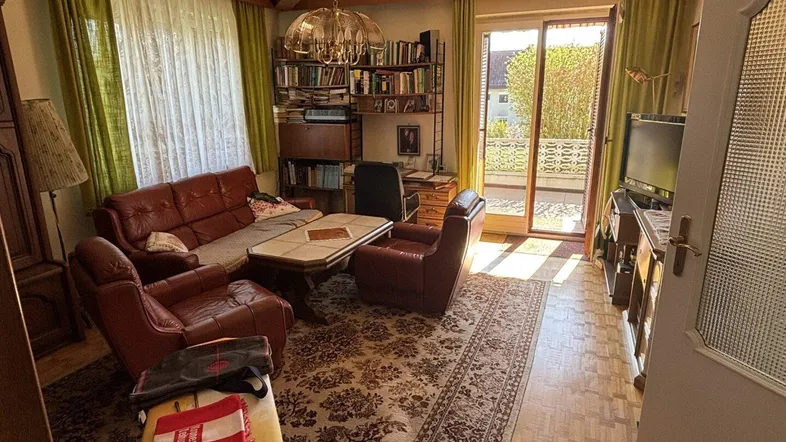 Gemütliches Wohnzimmer mit Ledersofas, Teppichboden und Zugang zu einem Balkon.