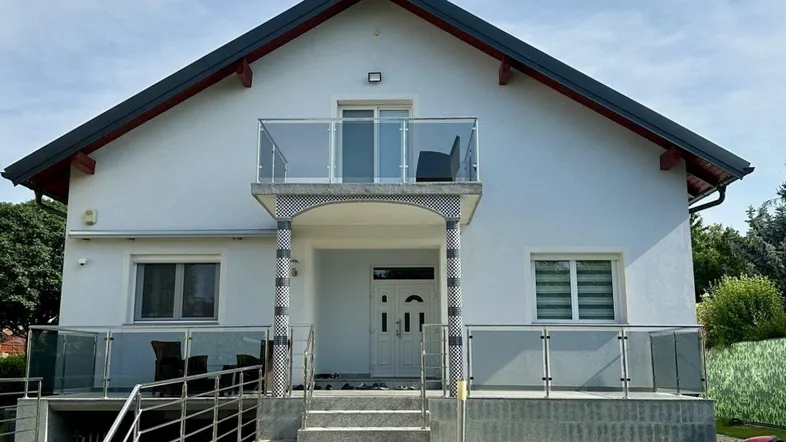 Moderne Hausfassade mit Balkon, Rampe und Treppenzugang zum Eingangsbereich.