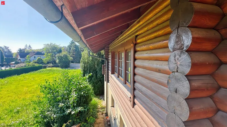 Nahaufnahme der rustikalen Holzfassade eines Blockhauses mit Blick ins Grüne.