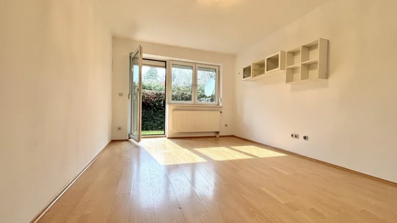 Helles Wohnzimmer mit Parkettboden, Zugang zum Garten und Tageslicht durch große Fenster.
