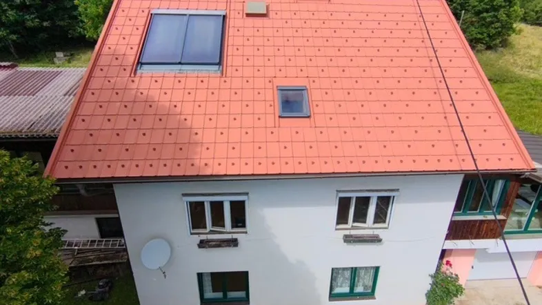 Das Haus präsentiert sich mit einem roten Ziegeldach, Solarpaneelen und einer weißen Fassade, umgeben von üppigem Grün.