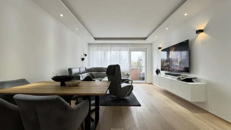 Heller, offener Wohn-Essbereich mit modernem Design, Holzboden und Zugang zum Balkon.