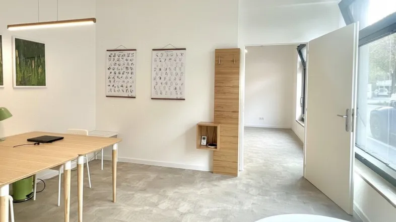 Moderner Büroraum mit hellen Wänden, Holztisch und funktionaler Einrichtung, ideal für kreatives Arbeiten.