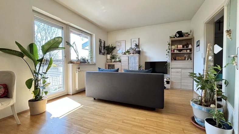 Helles Wohnzimmer mit Holzfußboden, großen Fenstern und viel Tageslicht.