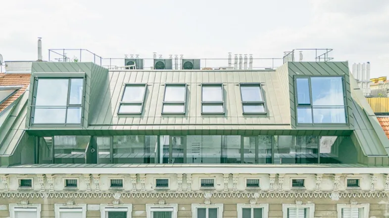 Moderne Dachgeschoss-Erweiterung auf einem historischen Gebäude mit großen Fenstern und Dachterrassen.