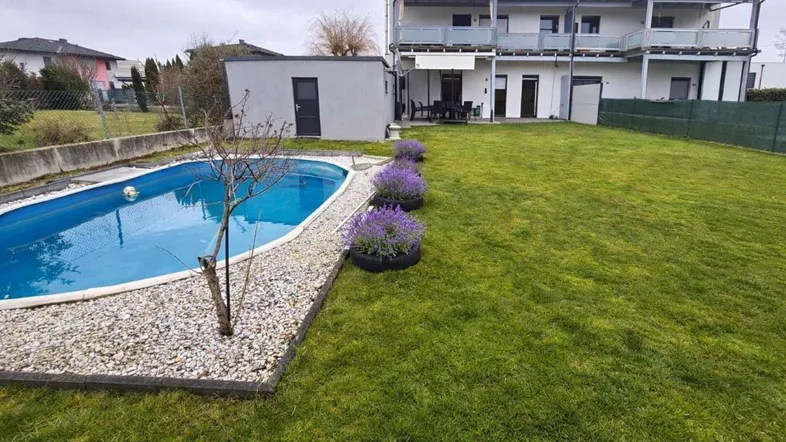 Großer Garten mit privatem Pool, Rasenfläche und moderner Wohnanlage im Hintergrund.