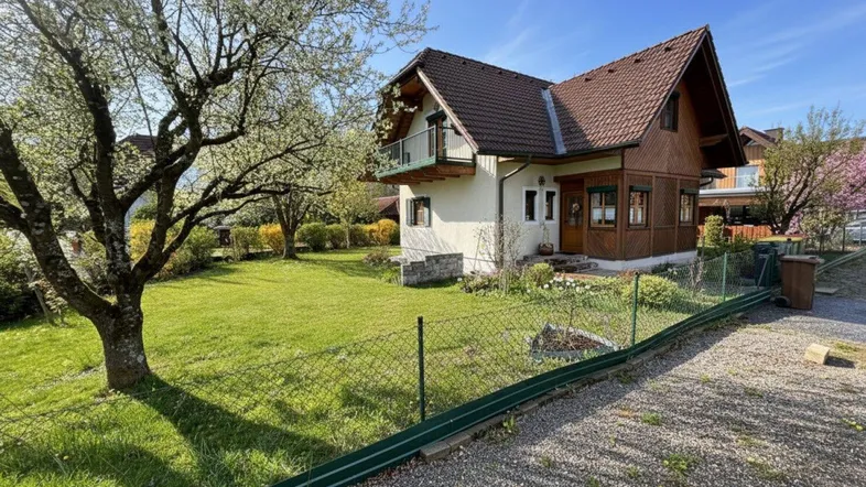 Charmantes Einfamilienhaus mit großem, gepflegtem Garten und blühenden Bäumen unter blauem Himmel.