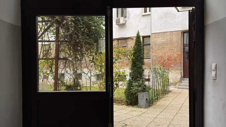 Eingangsbereich mit Glastür, die sich zu einem gepflasterten Innenhof mit Bäumen öffnet.