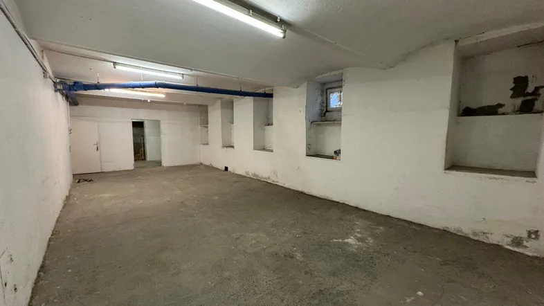 Geräumiger Kellerraum mit Betonboden, weiß gestrichenen Wänden und sichtbaren Rohren.